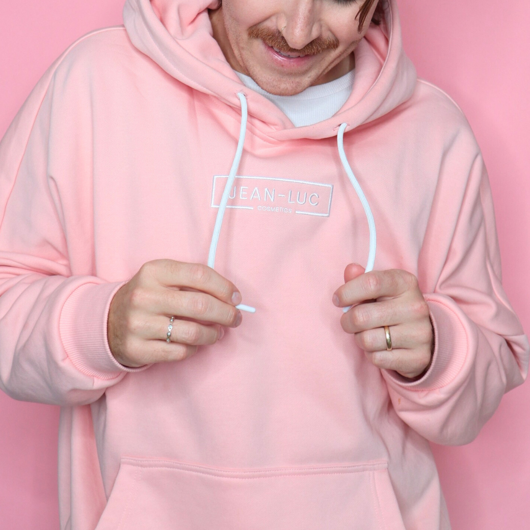 Person wearing a pink hoodie with a brand logo on a pink background