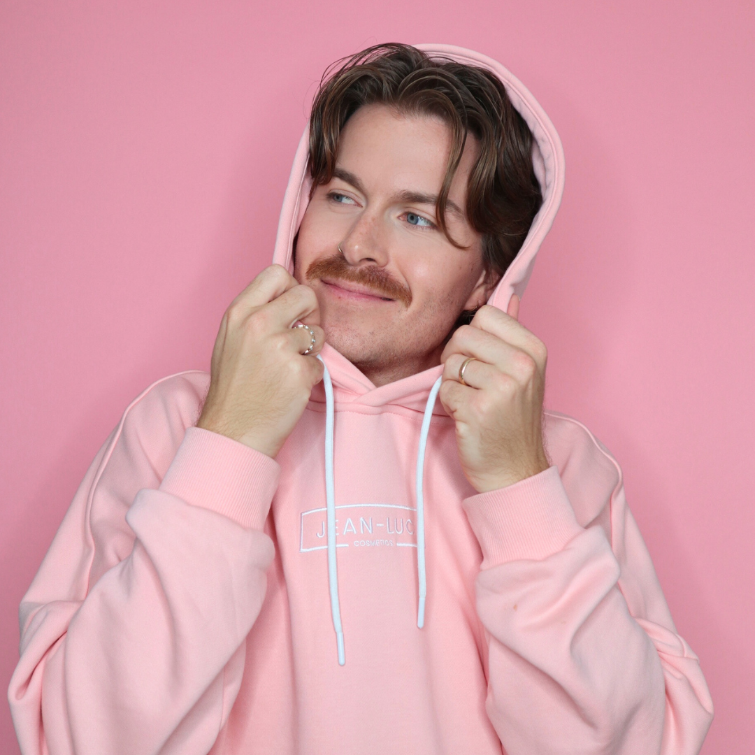 Person wearing a pink hoodie with a brand logo on a pink background
