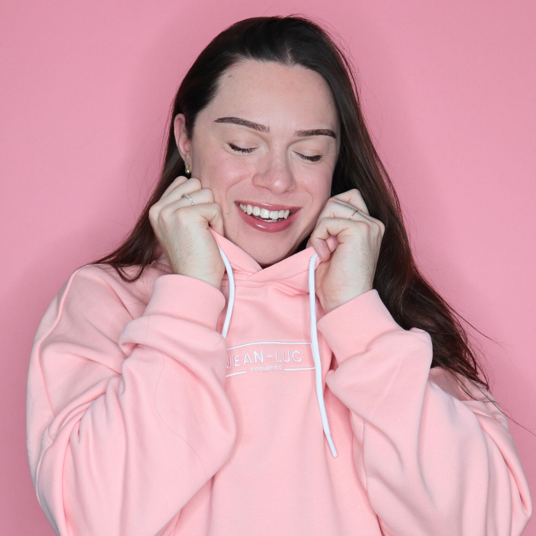 Woman wearing a pink hoodie with a brand logo against a pink background
